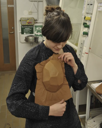 A woman with dark hair holding a large piece of leather shaped like a facetted stone.