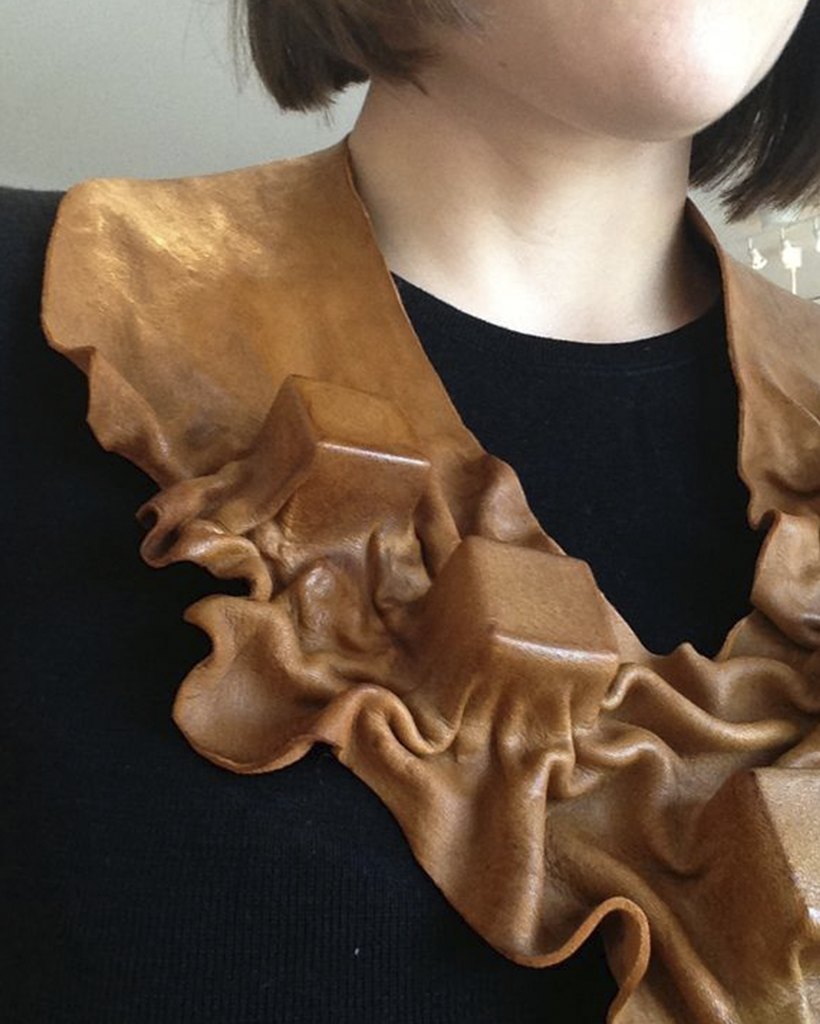 Close up of a wet molded brown leather neckpiece on a black sweater.